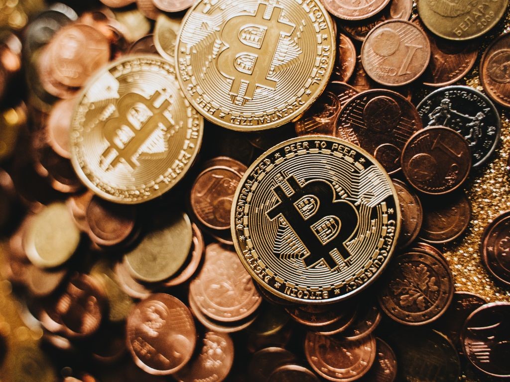 A pile of Bitcoin (BTC) coins interspersed with other currencies, representing cryptocurrency wealth.