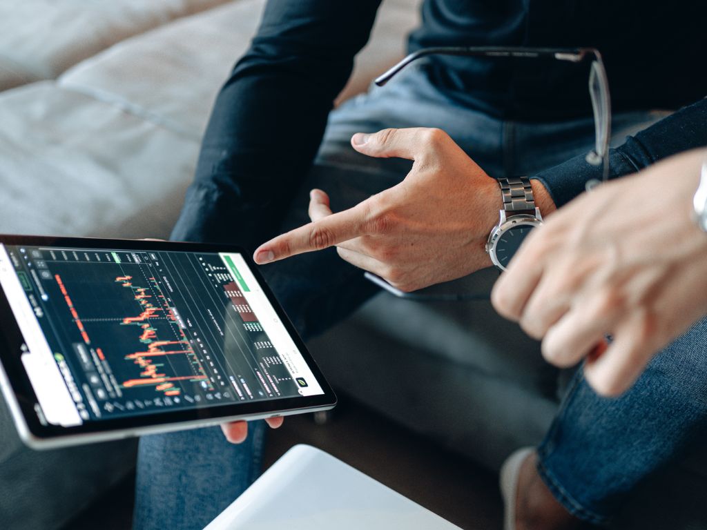 A close-up of two people pointing at a tablet displaying cryptocurrency market charts.